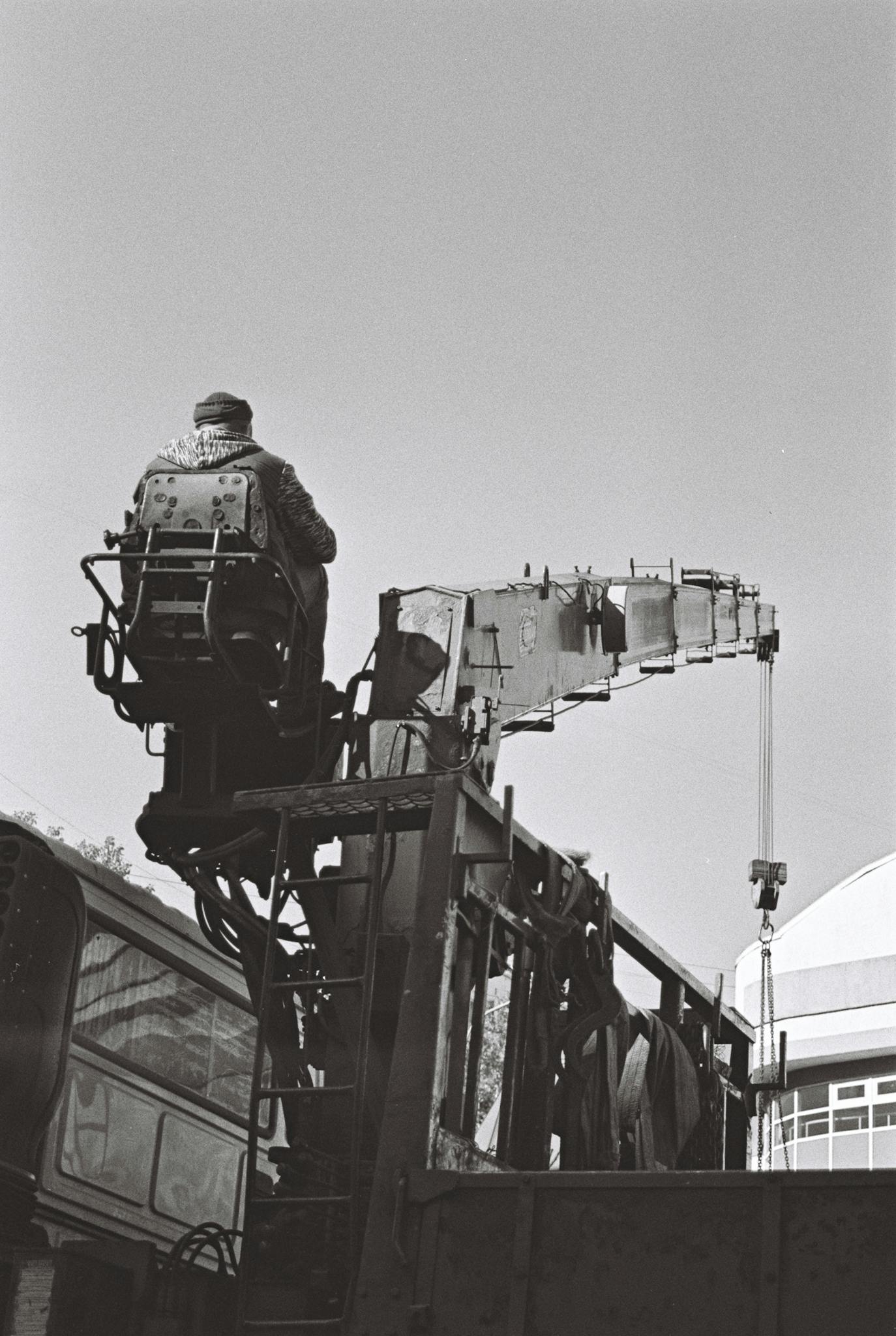 Black and white image of a crane operator working on site, showcasing industrial machinery.
