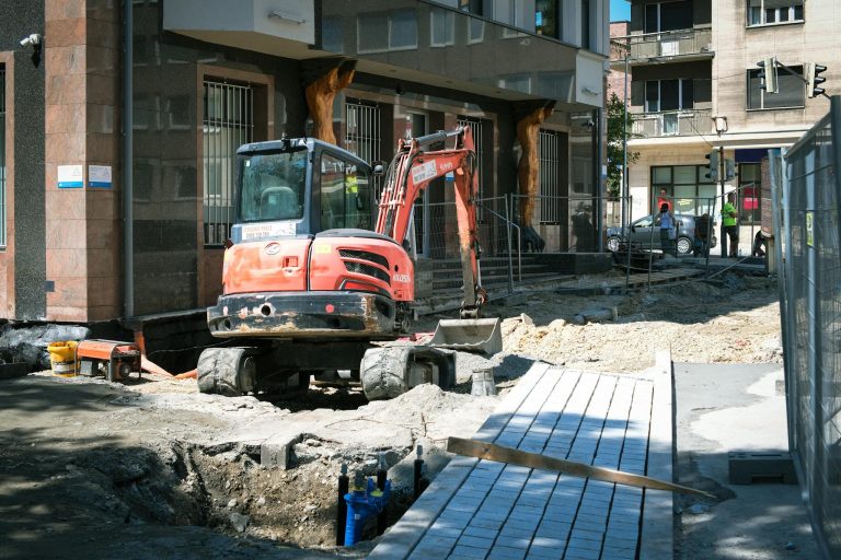 Street construction site in Bratislava with excavator and building.